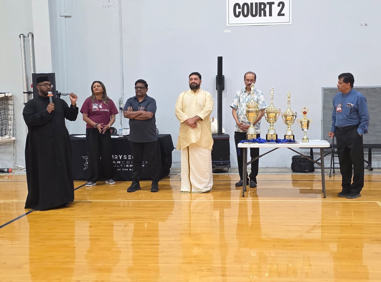 A speaker addresses the gathering beside the tournament trophies